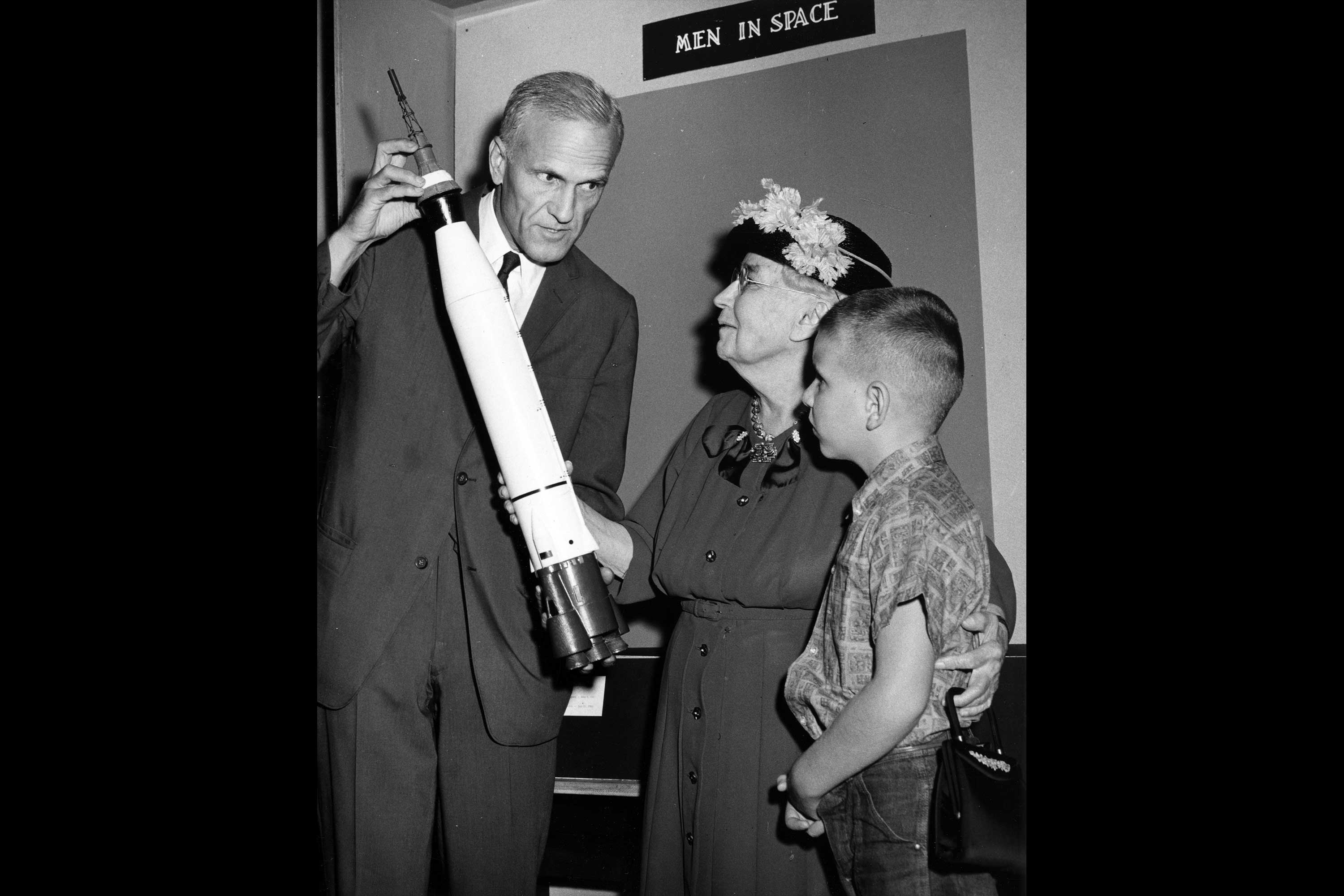 Brad Washburn with Atlas LV-3B. This is a photograph of three people looking at a model rocket.