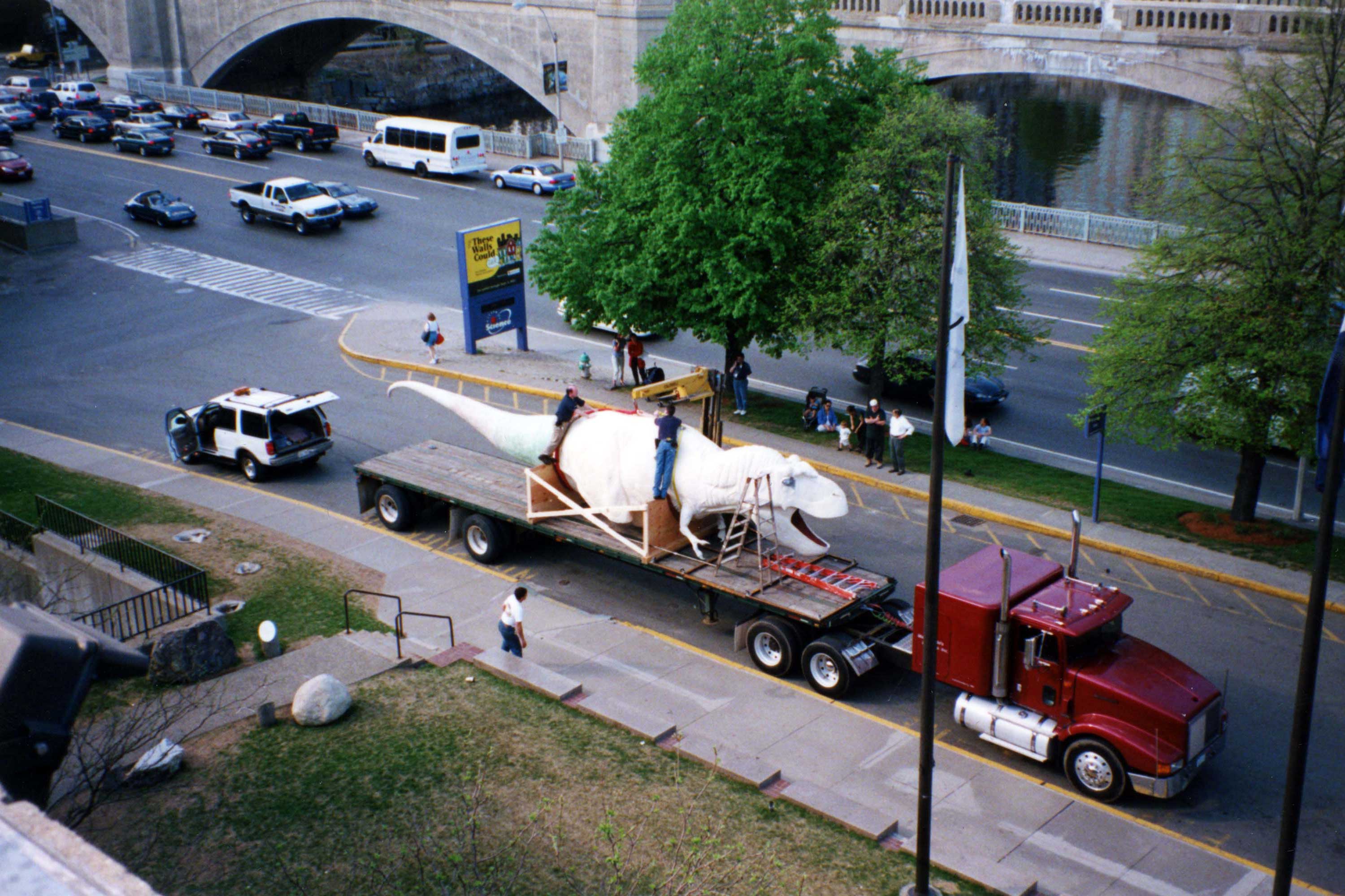 Current Model T.rex Delivery. This is a photograph of a life-size T. Rex model on a trailer that is partially built and unpainted.